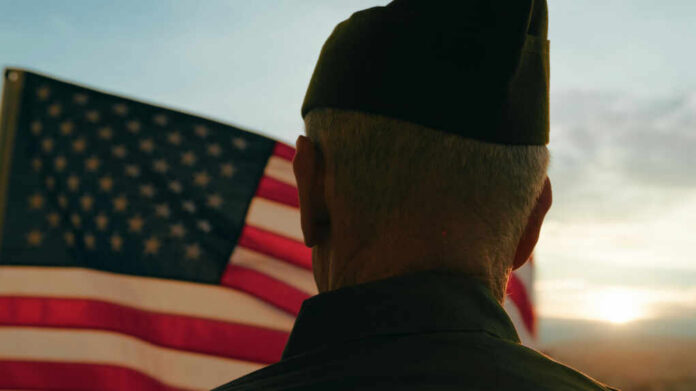 A veteran in uniform standing in front of an American flag during sunset