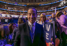 A smiling man in a suit at a political event surrounded by an engaged crowd