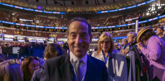 A smiling man in a suit at a political event surrounded by an engaged crowd