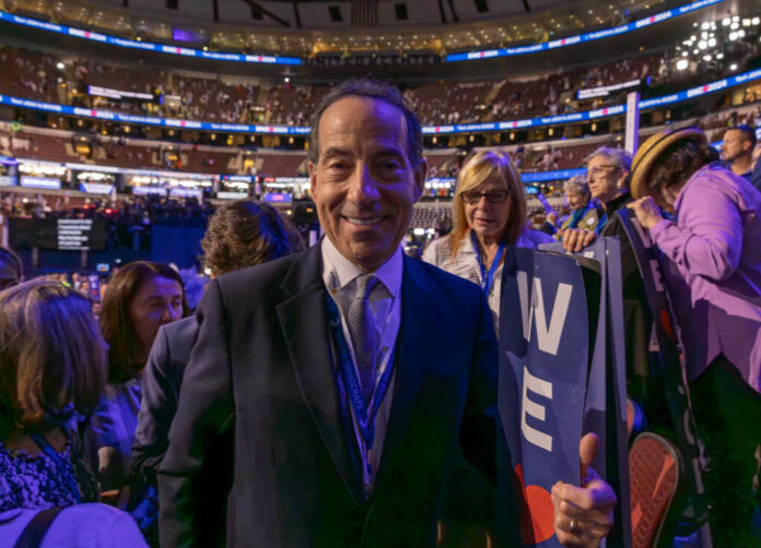 A smiling man in a suit at a political event surrounded by an engaged crowd