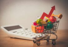A shopping cart filled with colorful grocery items next to a calculator and an upward trend arrow