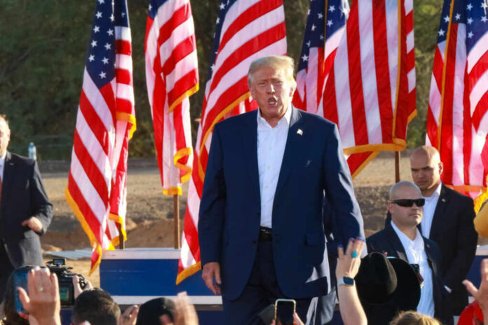 A speaker at a political rally surrounded by American flags and an engaged crowd