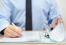 A person in a blue shirt writing on a document while holding a binder