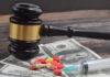 A gavel placed on top of money with pills and a syringe nearby