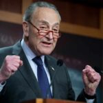 A senator passionately speaking at a press conference with raised fists