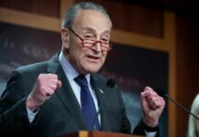 A senator passionately speaking at a press conference with raised fists
