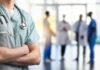 A healthcare professional in scrubs with a stethoscope, standing with arms crossed in a hospital setting