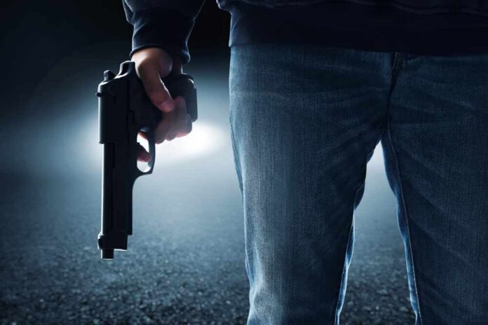Hooded,Man,Holding,A,Gun,On,Urban,City,Alley,Street A person holding a handgun in a dark environment