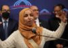A woman in a hijab passionately speaking at a podium during a public event