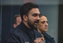 A man in a mayor's jacket speaking at a press conference with a woman in the background