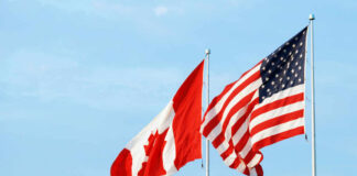 Canadian and American flags waving against a blue sky