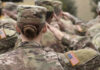 Female soldier saluting during a military ceremony with fellow soldiers in camouflage uniforms