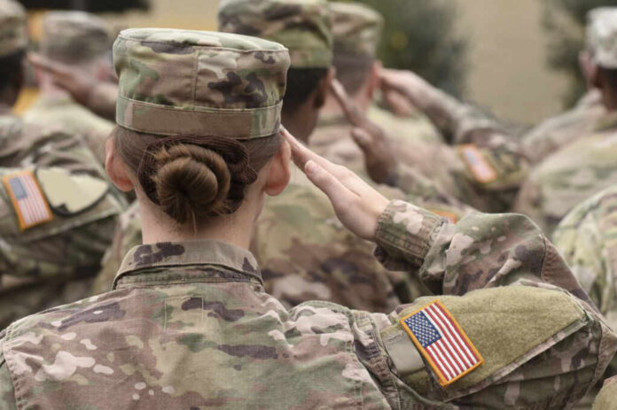 Female soldier saluting during a military ceremony with fellow soldiers in camouflage uniforms