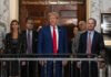 Election Saved Trump, AG Hints A group of individuals, including a political figure, standing in front of a courtroom entrance