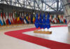 EU Draws Line On Fighting-Age Men Flags of European countries displayed in a modern hall with a red carpet