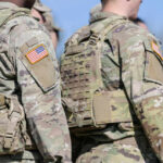 Military personnel in camouflage uniforms with U.S. flag patches standing outdoors
