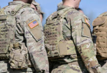 Military personnel in camouflage uniforms with U.S. flag patches standing outdoors