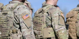 Military personnel in camouflage uniforms with U.S. flag patches standing outdoors