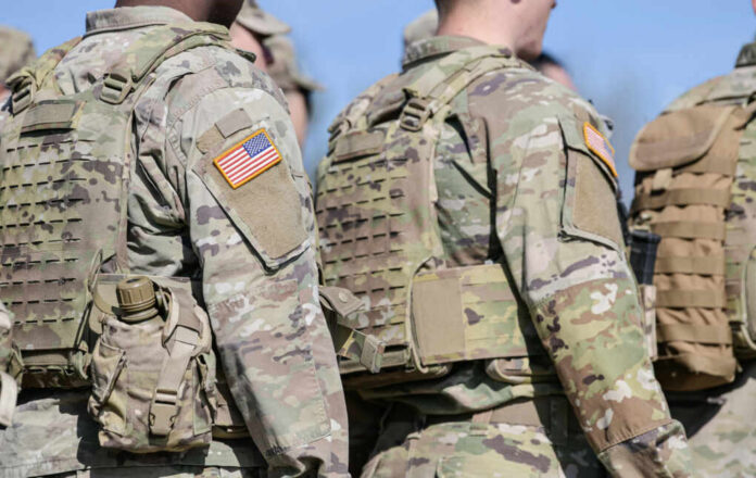 Military personnel in camouflage uniforms with U.S. flag patches standing outdoors