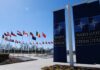 Europe’s NATO Breakup Talk Escalates Flags of various nations displayed outside NATO headquarters under a clear blue sky