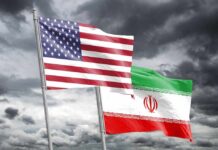 Flags of the United States and Iran waving against a cloudy sky