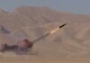 1,000-Mile Missile — Fantasy Or Fiscal Fiasco? A missile launching into the sky with smoke and flames in a desert setting