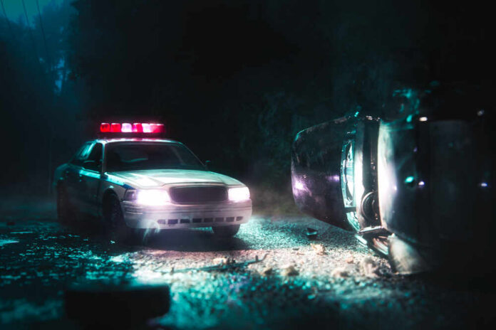High,Contrast,Image,Of,A,Police,Car,Arriving,Near,A A police car with flashing lights at the scene of a flipped vehicle accident