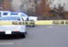 Police tape cordons off a street with patrol cars in the background