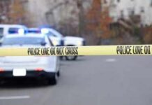 Police tape cordons off a street with patrol cars in the background
