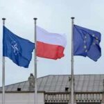 Mystery Factory Hides Inside Poland’s Tank Deal Three flags on poles including NATO, Poland, and the European Union