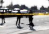 ICE Gunfire Sparks Maine Uproar Police tape cordons off a street with blurred officers and vehicles in the background