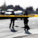Police tape cordons off a street with blurred officers and vehicles in the background