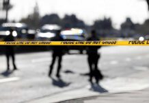 Police tape cordons off a street with blurred officers and vehicles in the background