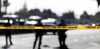 Police tape cordons off a street with blurred officers and vehicles in the background