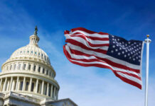 American flag waving in front of the U.S. Capitol building under a clear blue sky