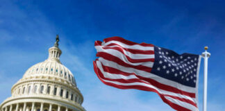 American flag waving in front of the U.S. Capitol building under a clear blue sky