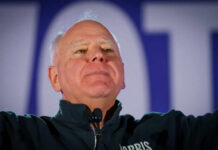 Man in a dark jacket speaking passionately at a podium with a microphone