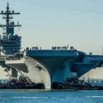 Aircraft carrier guided by tugboats in a harbor