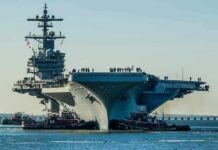 Carrier Repaired, Retirement Looms—Why? Aircraft carrier guided by tugboats in a harbor
