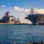 Aircraft carrier and support ships docked at a naval harbor