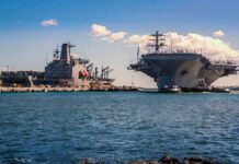 Aircraft carrier and support ships docked at a naval harbor
