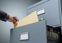 Hand filing a manila folder into an open metal filing cabinet drawer