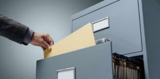 Hand filing a manila folder into an open metal filing cabinet drawer