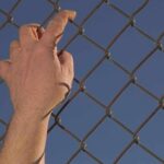 Hand gripping a chain-link fence