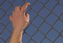 Border Mayhem Strands Hundreds Of Children Hand gripping a chain-link fence