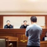 defendant stands before judges in a courtroom