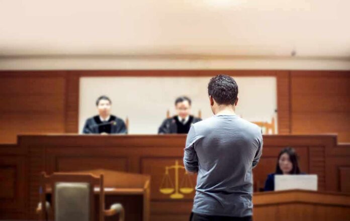 defendant stands before judges in a courtroom