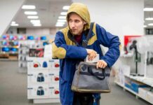 Person in hooded jacket placing item into a gray bag in a store aisle