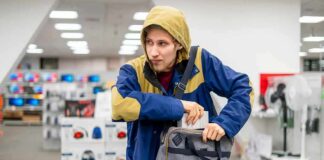 Person in hooded jacket placing item into a gray bag in a store aisle