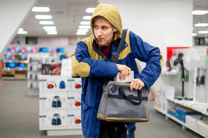 Person in hooded jacket placing item into a gray bag in a store aisle